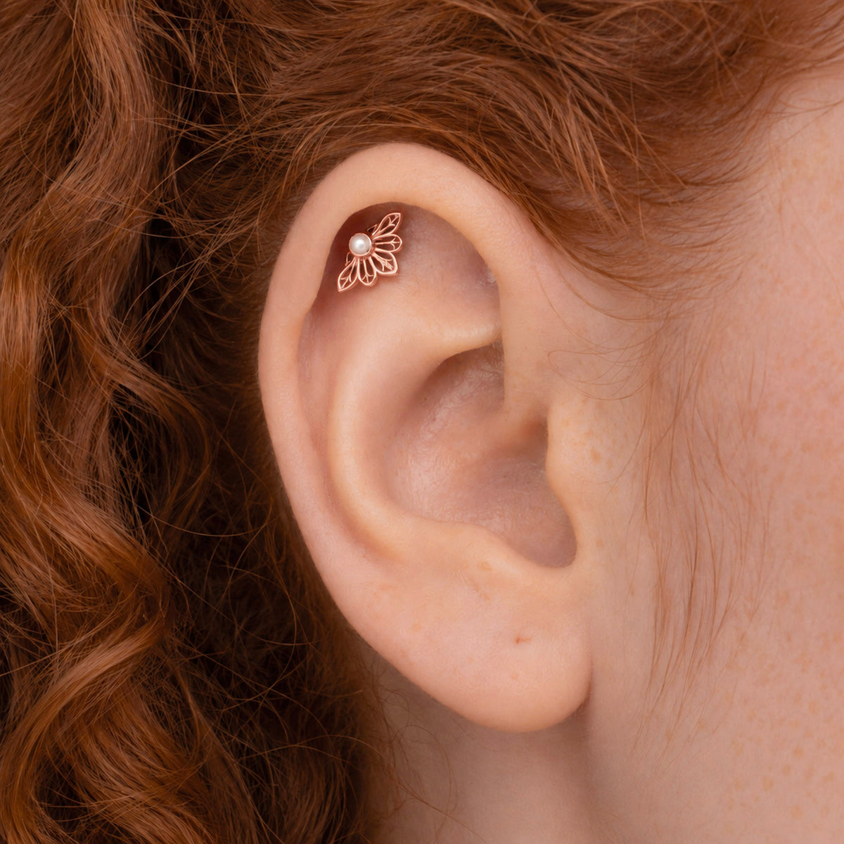 Rose gold flower-shaped helix piercing with a small pearl on a human ear
