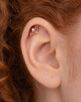 Rose gold flower-shaped helix piercing with a small pearl on a human ear