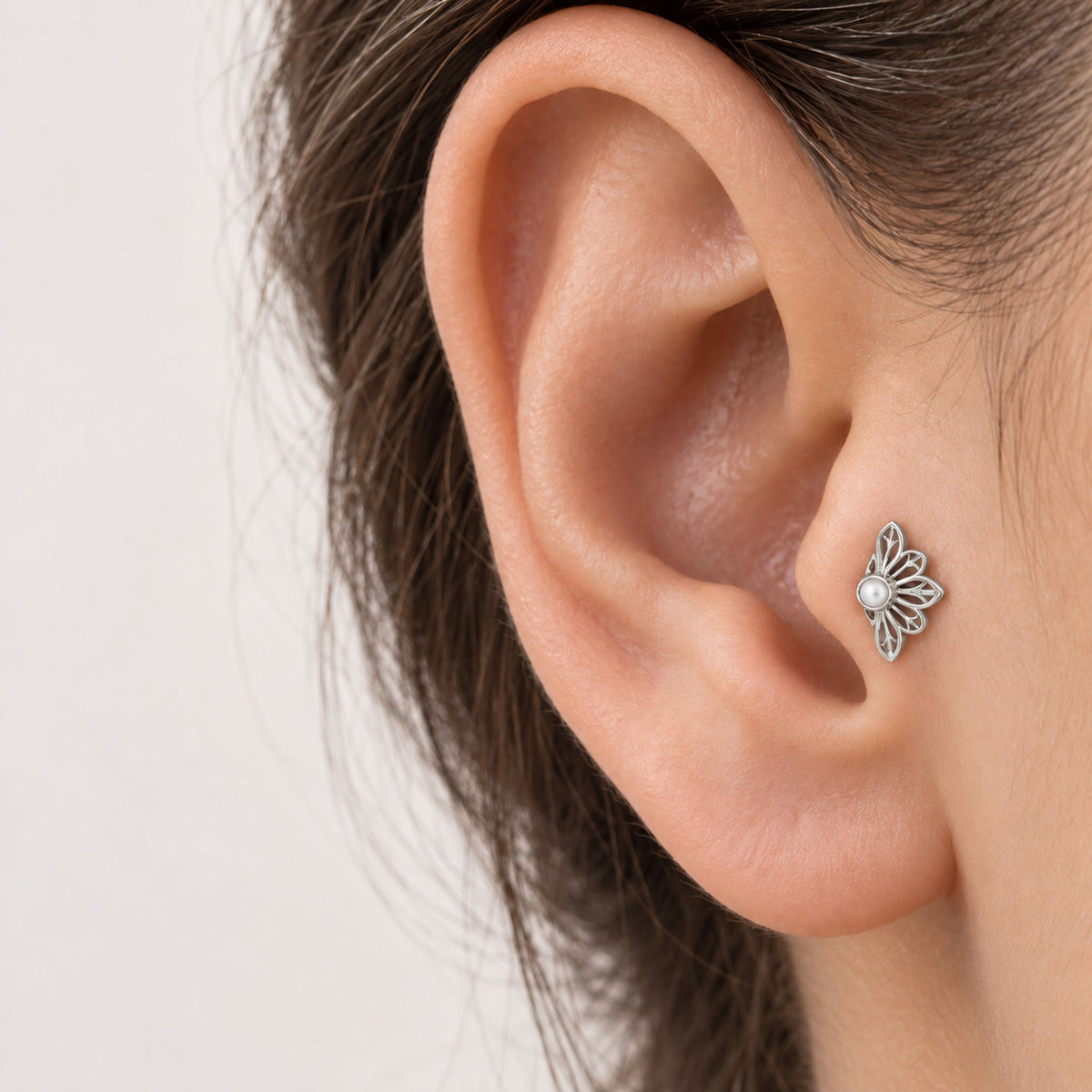 Close-up of a silver flower-shaped stud earring with a pearl center in an ear piercing.