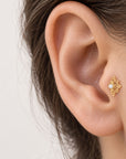 18k gold flower-shaped stud earring with a small pearl in a woman's ear lobe