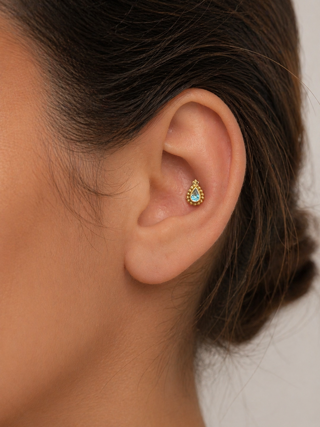 Close-up of ear with gold and blue gemstone piercing, handmade ethical 18k gold jewelry