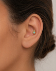 Close-up of ear with gold and blue gemstone piercing, handmade ethical 18k gold jewelry