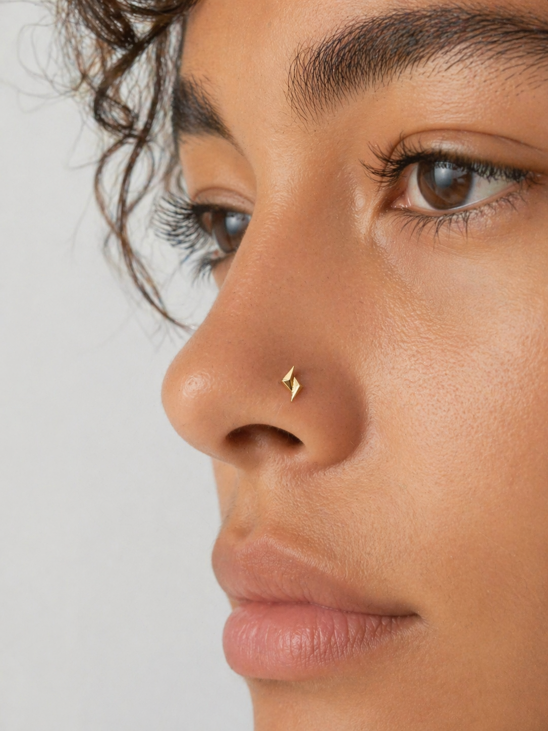 Close-up of a woman wearing a minimalist gold nose stud piercing
