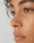 Close-up of a woman wearing a minimalist gold nose stud piercing