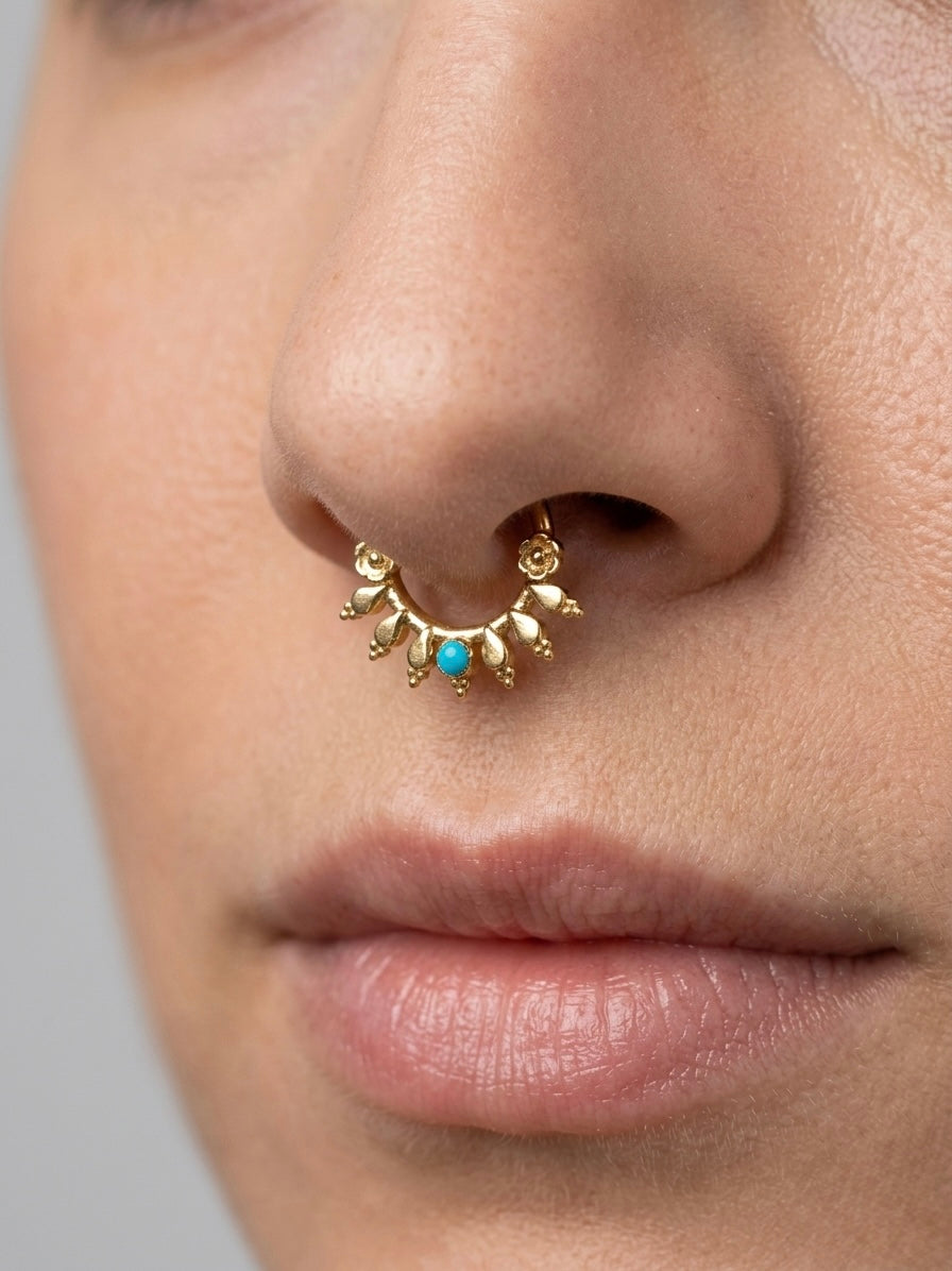 Close-up of a nose with a gold septum piercing featuring a turquoise stone and leaf details