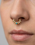 Close-up of a nose with a gold septum piercing featuring a turquoise stone and leaf details