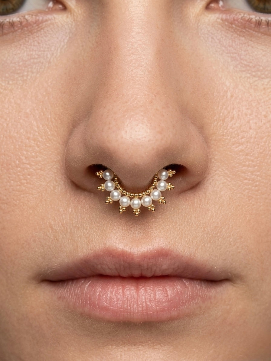 Close-up of a nose with a gold septum piercing adorned with small pearls.