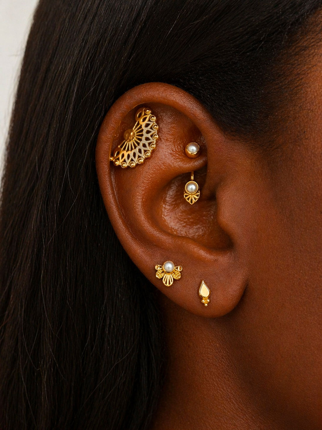 Close-up of ear with multiple 18k gold and pearl piercings, intricate luxury jewelry