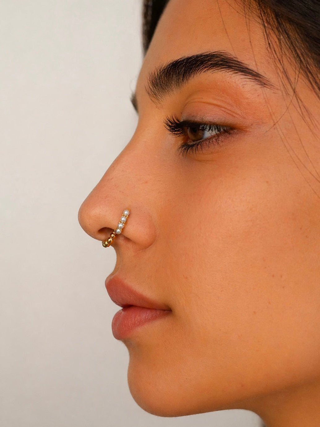 Close-up of woman wearing 18k gold nose ring with pearls and gemstones