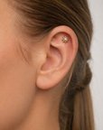 Close-up of ear with 18k gold sun-shaped cartilage piercing with pearl center