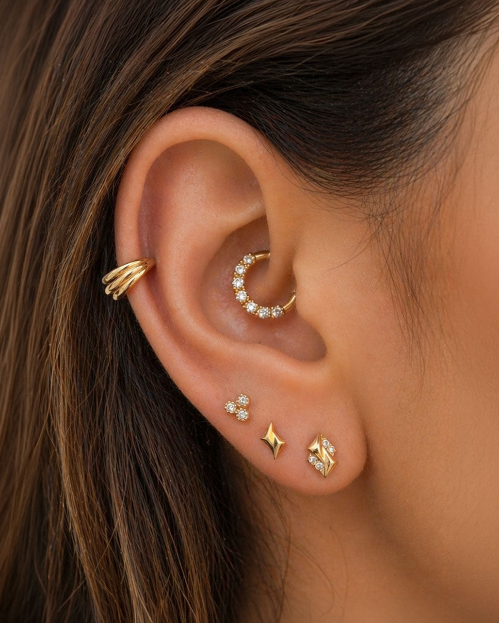 Ear with multiple gold and diamond piercings, including hoops and studs, close-up view