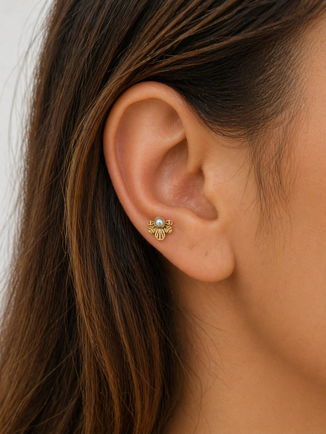 Close-up of ear with 18k gold piercing featuring a pearl and intricate gold detailing