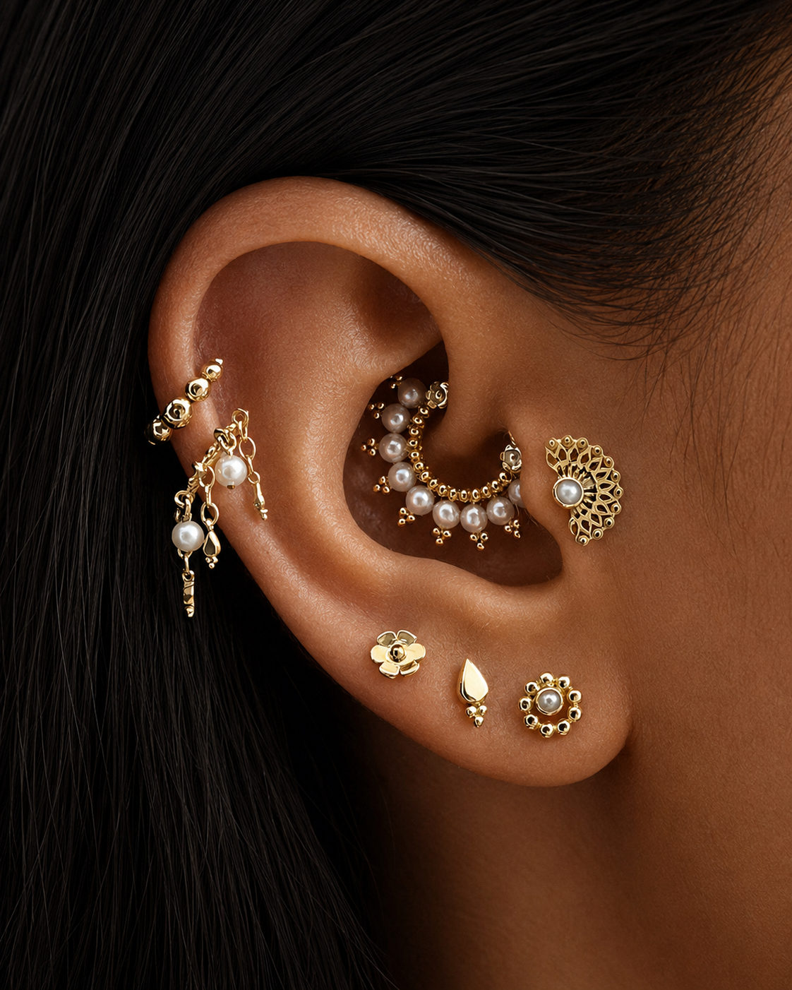 Close-up of ear with multiple 18k gold piercings, pearl accents, and intricate luxury jewelry.