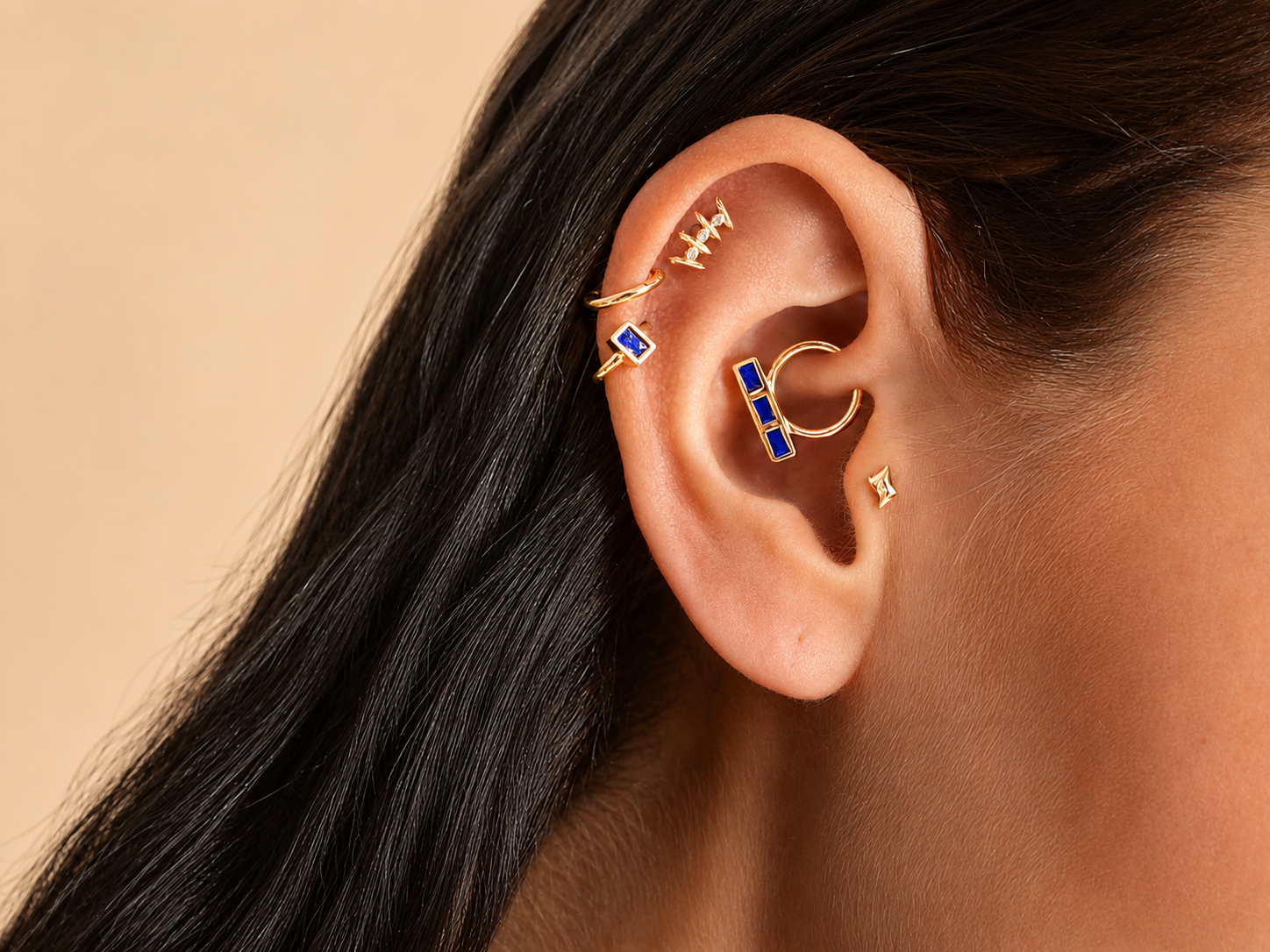 Close-up of ear with multiple 18k gold piercings and blue gemstone jewelry