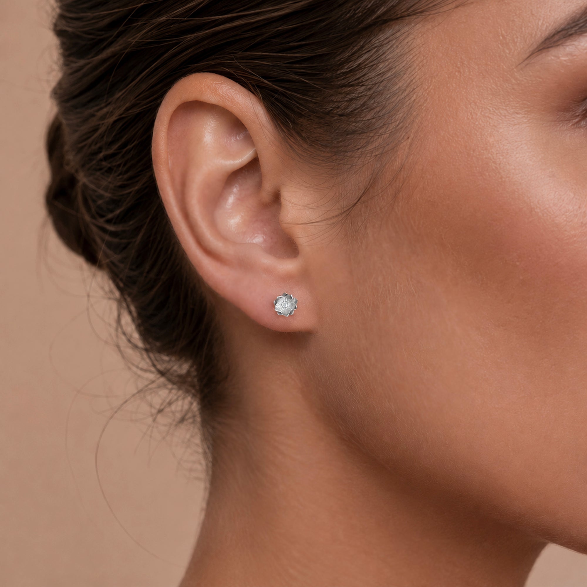 Delicate flower stud earring in 18k gold with diamond center, worn on earlobe for elegant piercing jewelry look