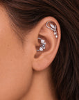 Close-up of a person's ear with silver floral and leaf motif ear cuffs and pearl accents.