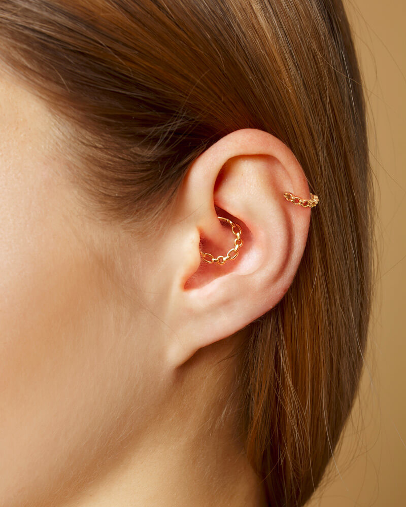 Close-up of ear with two gold chain cartilage piercings, minimalist jewelry style